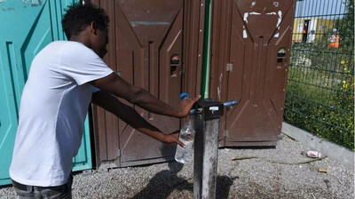 Un jeune homme remplit une bouteille au robinet installé près d'un campement, en juillet 2019. Ce lieu de vie a, depuis, été évacué. Crédit : InfoMigrants